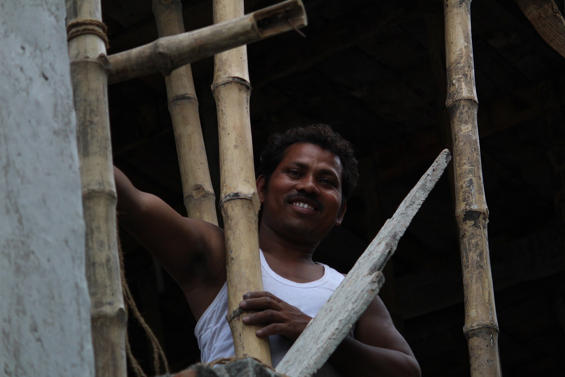 A smiling man works on a bamboo structure during construction, highlighting the realities of India's informal economy.