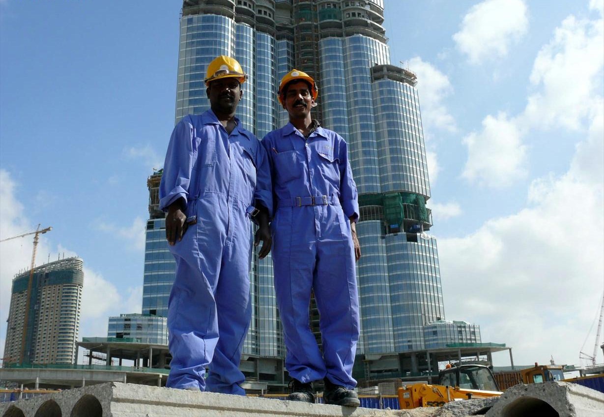 Gulf Migration | Indian Press Construction workers are silhouetted against a skyscraper, illustrating migration and labor in the Gulf region.