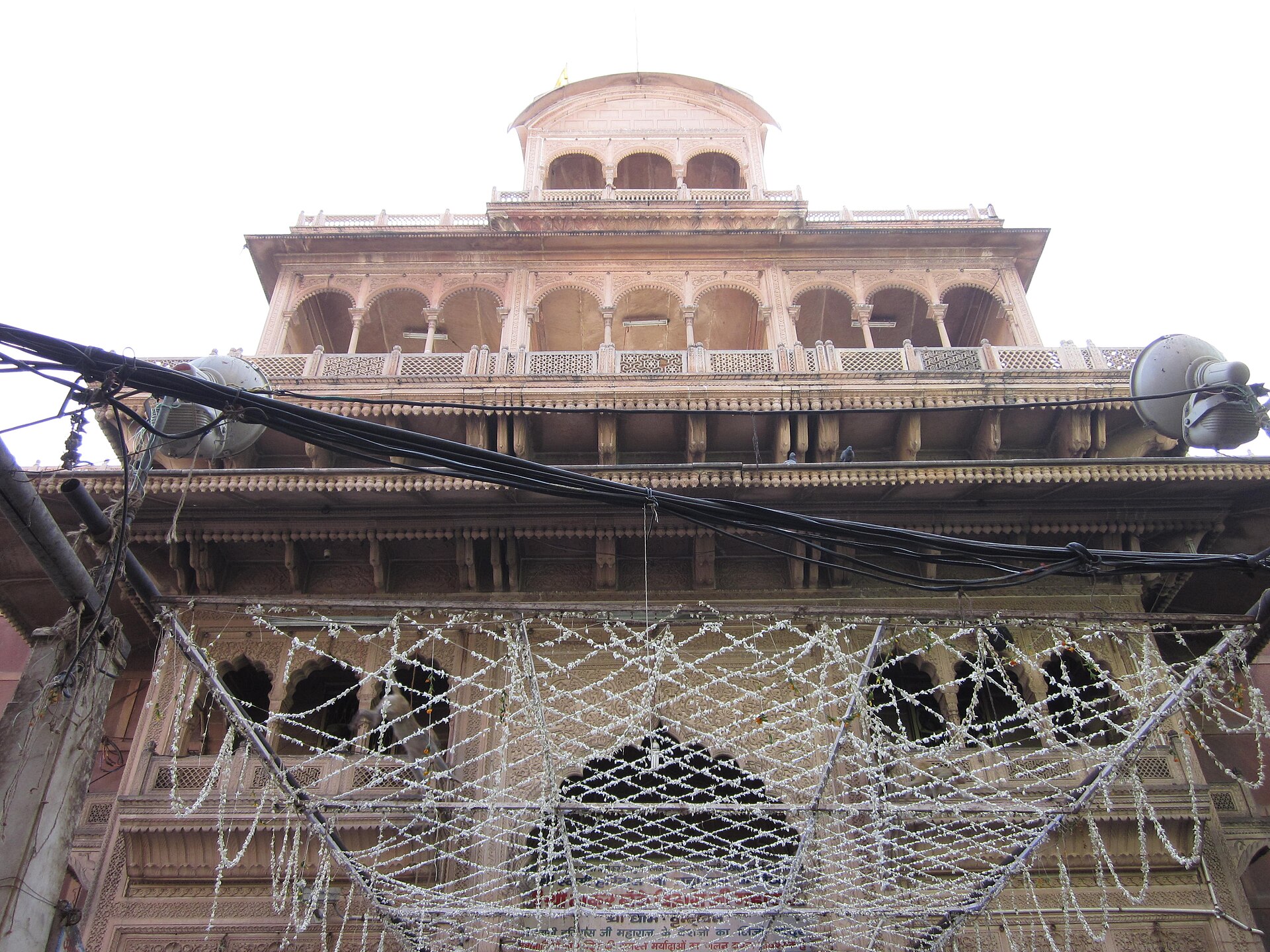 Holi | Indian Press An ornate pink building with carvings and security fencing represents Holi celebrations in India.