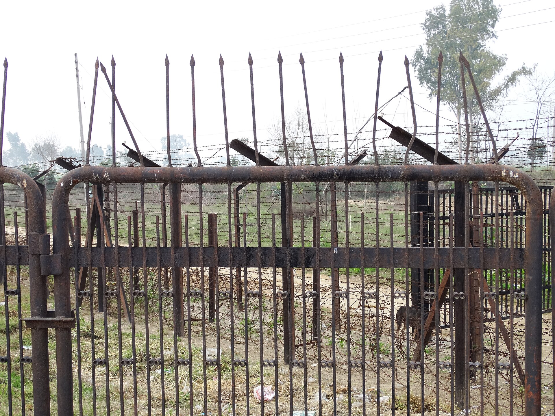 India-Pakistan Border | Indian Press A rusty metal gate and barbed wire fencing marks the boundary between India and Pakistan, illustrating a poignant history.