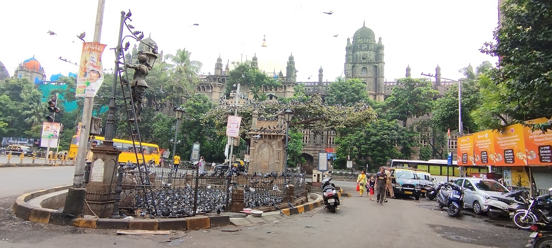 A historic gateway and monument are seen amidst a bustling city street, illustrating India's long postal history.