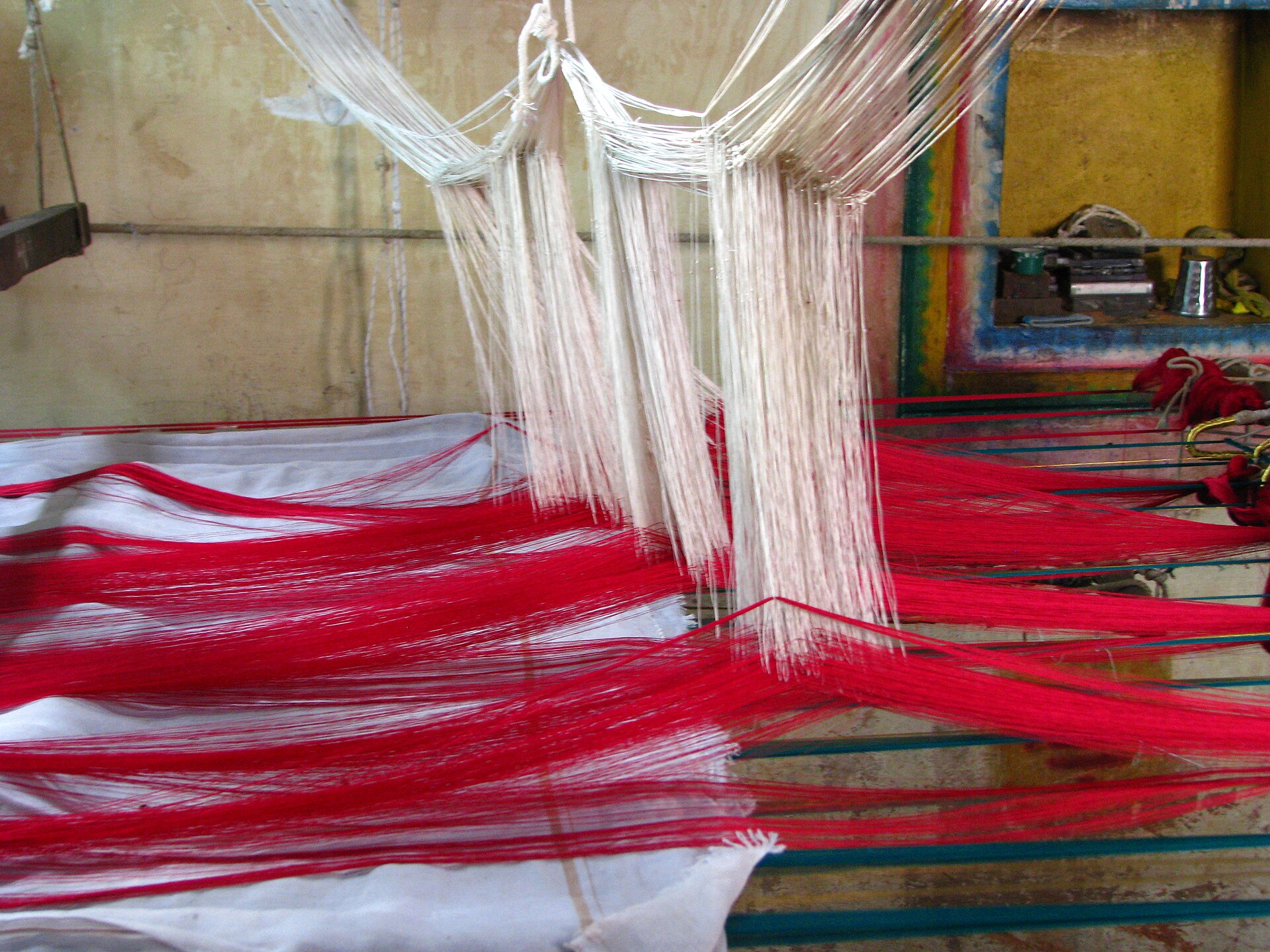 Kanchipuram Sari Weaving | Indian Press A traditional handloom weaves a vibrant red and white textile, showcasing Indian crafts.