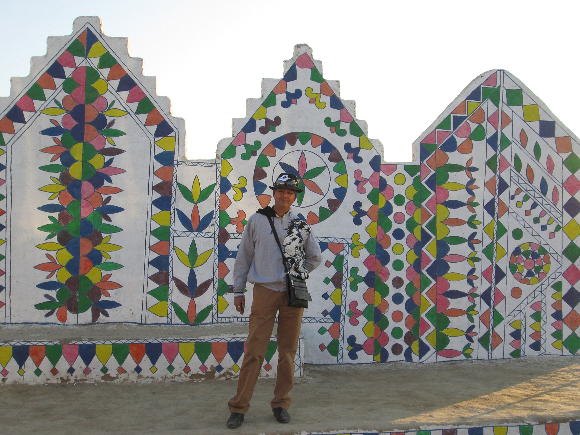 A man stands before a vibrantly painted wall at the Ahmedabad Kite Festival, showcasing Indian culture.