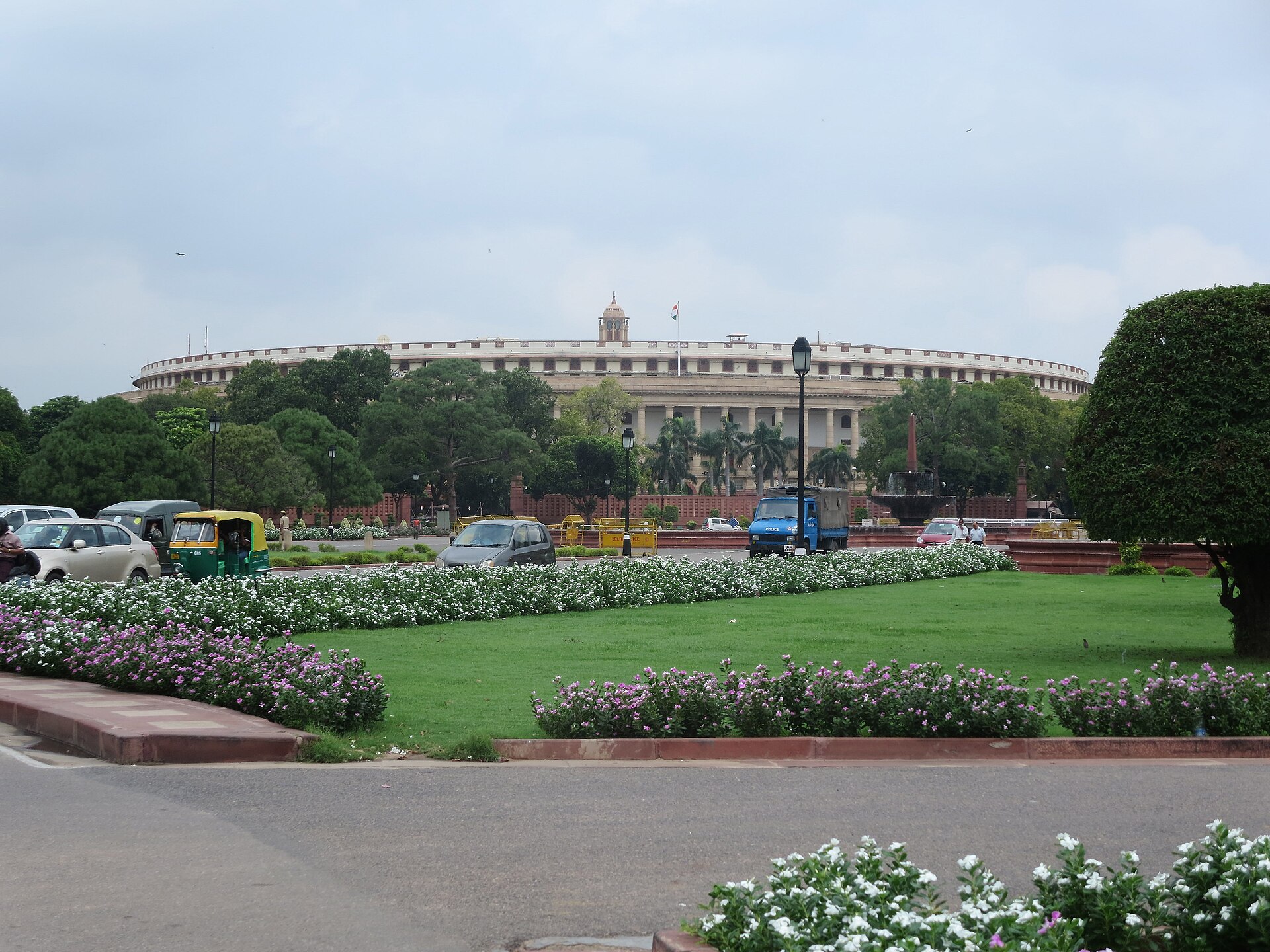 New Delhi Parliament | Indian Press Parliament House in New Delhi is surrounded by greenery and a vibrant flowerbed, reflecting India's culture.