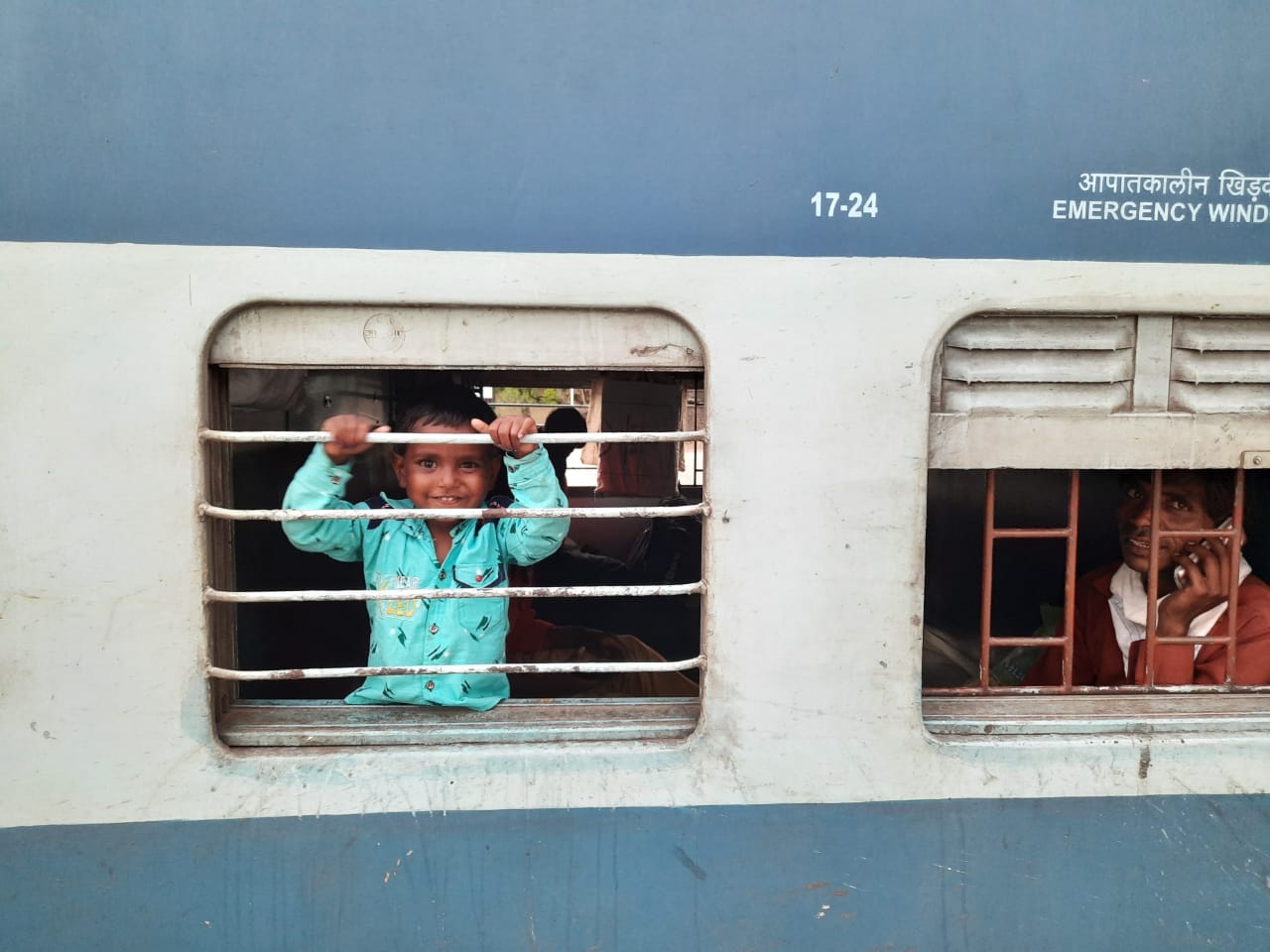 Seasonal Migration | Indian Press A child peers out a train window during seasonal migration in India, highlighting the challenges of transportation.